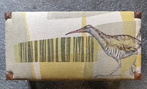 Image of the top of a stool covered in fabric with a print of a bird on abstract background 